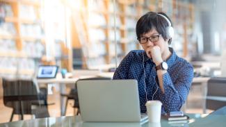 Person sitting at table with headphones on, typing on computer.